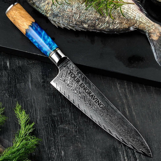 8 inch engraved Damascus chef knife with blue resin and pakka wood handle on dark wood surface with fresh fish and herbs