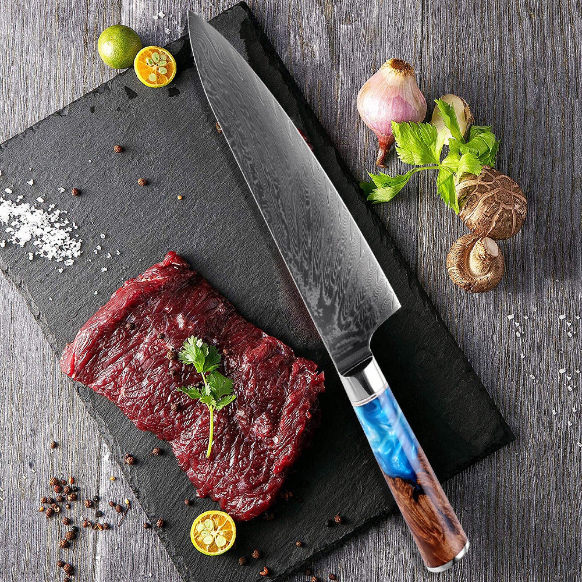 8 inch engraved Damascus chef knife with blue resin and pakka wood handle on dark wood surface with fresh fish and herbs